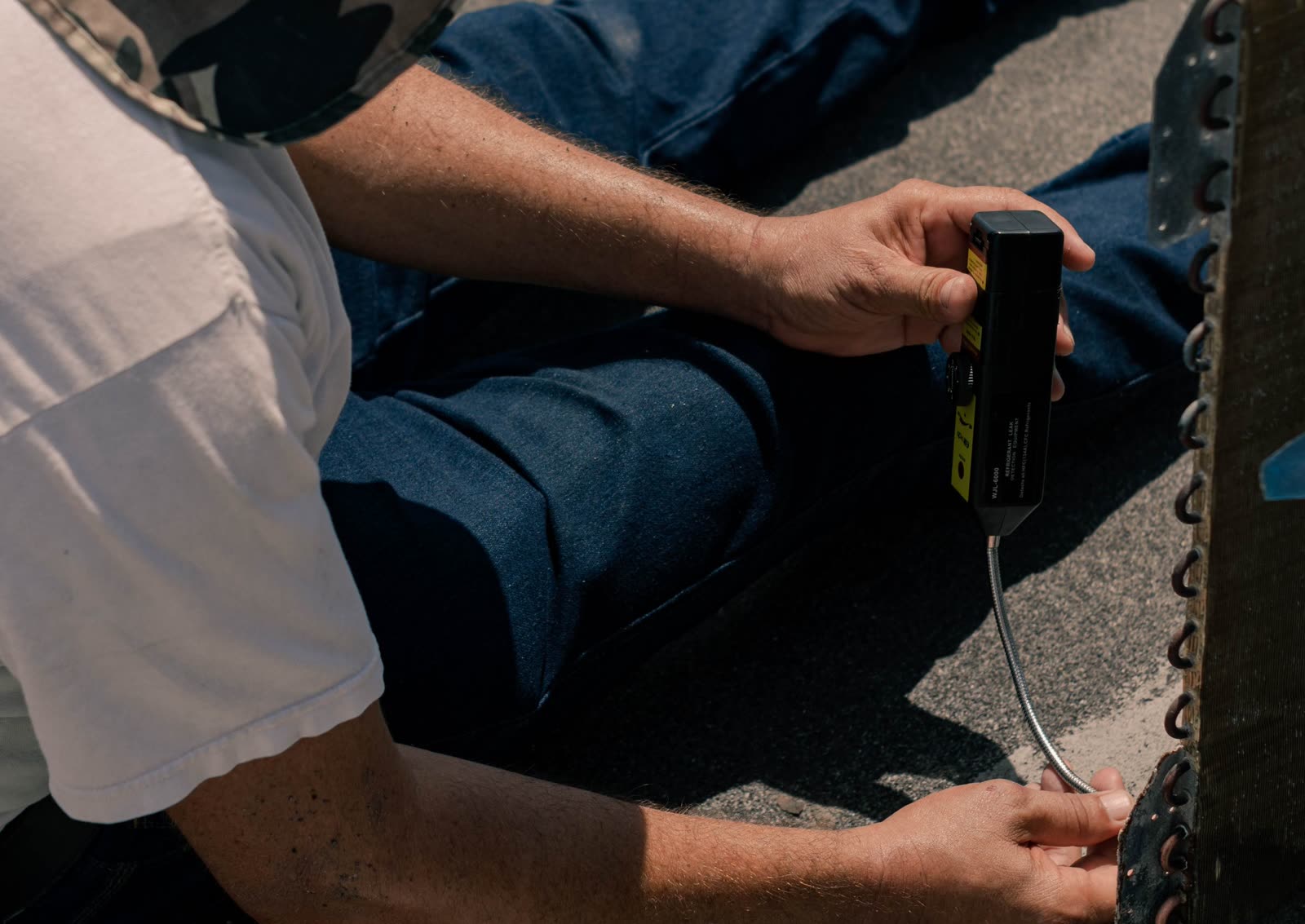 AC technician running an electronic leak detector along an air conditioner coil